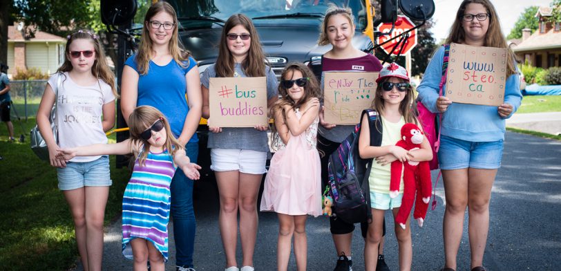 eight female students standing in front of parked bus holding various signs