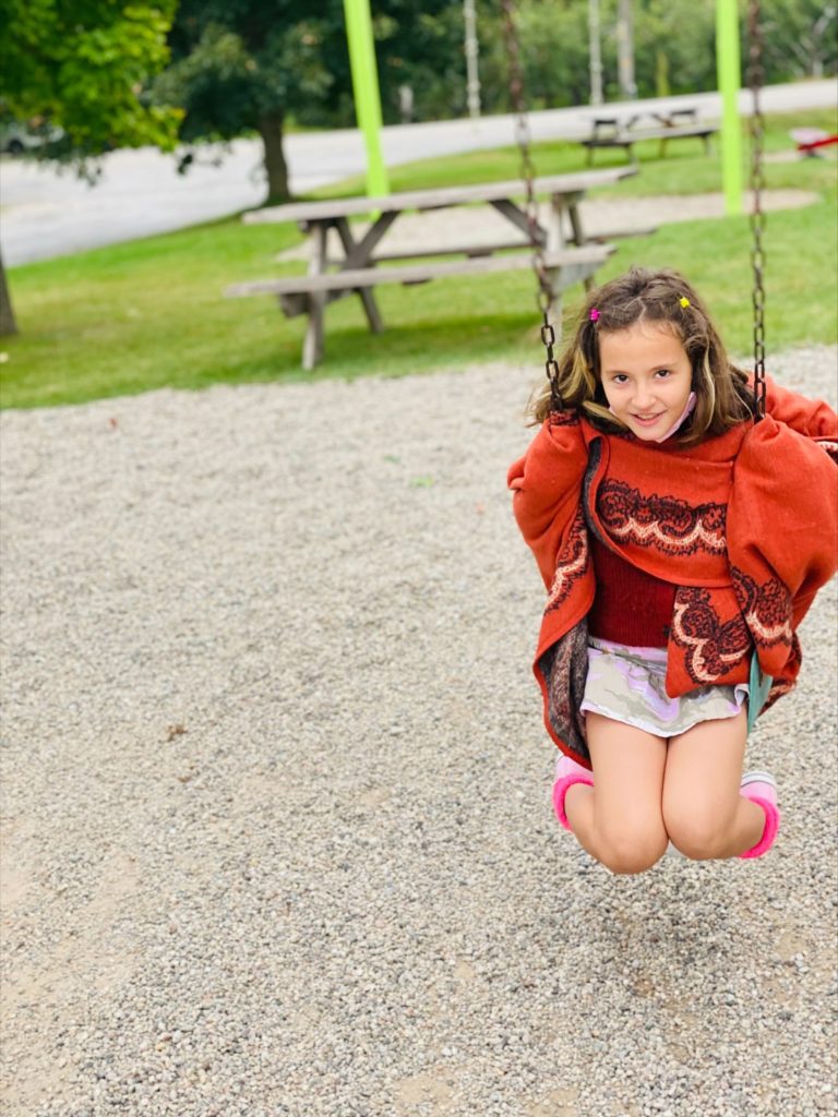 female student with a red sweater swinging on a swing set